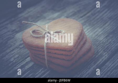 Ingwer-Plätzchen mit einem Seil von Flachs gebunden.  Lebkuchen Herz-förmig auf Holztisch. Kaffeepause, Frühstück. Weich, blau für Kopie Text Inserti getönten Stockfoto