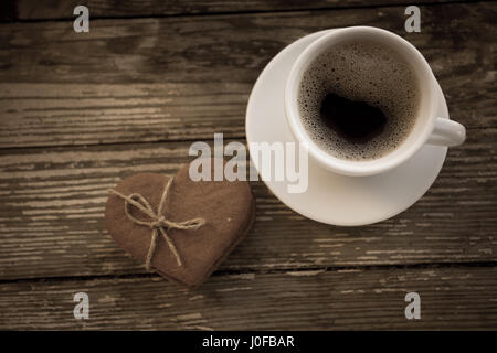 Tasse Kaffee mit Ingwer-Plätzchen auf Holztisch. Herzform Lebkuchen. Kaffeepause, Frühstück. Stockfoto