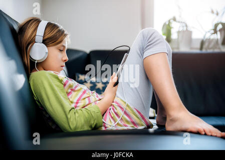 Mädchen sitzen auf schwarzes Sofa mit Tablet und Musik hören Stockfoto