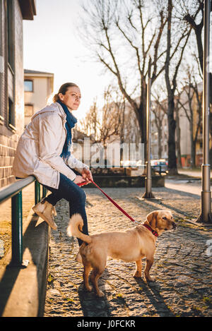 Frau mit einem Hund sitzt auf einem grünen Zaun Stockfoto