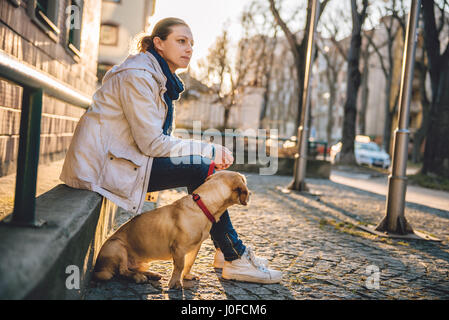 Frau mit einem Hund sitzt auf einem grünen Zaun Stockfoto