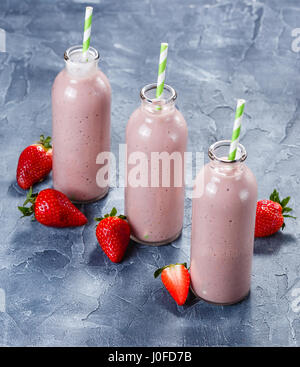 Erdbeer-Banane Smoothie in drei Flaschen und frische Erdbeeren auf einem hellblauen Hintergrund Stockfoto