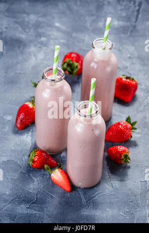 Erdbeer-Banane Smoothie in drei Flaschen und frische Erdbeeren auf einem hellblauen Hintergrund Stockfoto
