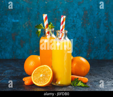 Orange und Karotten-Saft in Flaschen, Orangen und Baby-Karotten auf einem dunkelblauen Hintergrund Stockfoto