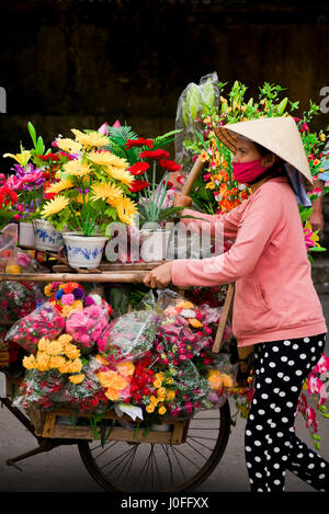 Vertikale Porträt einer Dame, Verkauf von Blumen von der Rückseite eines Fahrrades in Hoi an, Vietnam. Stockfoto