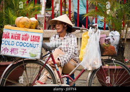 Horizontale Porträt einer Dame verkaufen kalt ganze Kokosnüsse von der Rückseite eines Fahrrades in Hoi an, Vietnam. Stockfoto