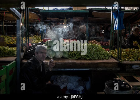 SKOPJE, Mazedonien - 24. Oktober 2015: Mann verkaufen Kohl und Paprika auf Skopje Markt Rauchen einer Zigarette in der Abenddämmerung Bild von einem Mann mittleren Alters smok Stockfoto