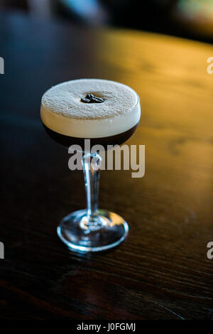 Ein einziges Glas Espresso martini mit Kaffeebohnen und Schaum auf einem Bartop Stockfoto