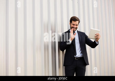 lächelnder Mann mit Anzug und Krawatte, mit einem virtuellen Gespräch auf seinem Tablet außerhalb Stockfoto