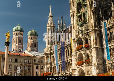 Detail des Rathauses am Marienplatz mit der Statue der Jungfrau Maria. Im Hintergrund die mächtigen Türme der Kirche Frauenkirche. Stockfoto