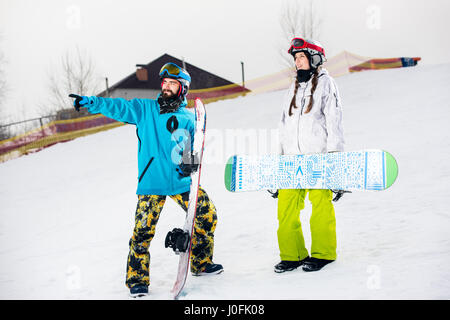 Junges Paar von Snowboardern stehen mit Snowboards auf Schnee und wegsehen Stockfoto