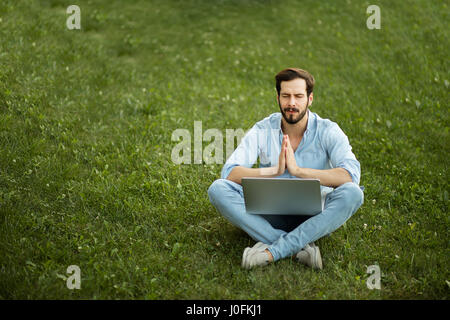 junger Mann liegen in der Wiese mit seinem Laptop vor draußen beten Stockfoto