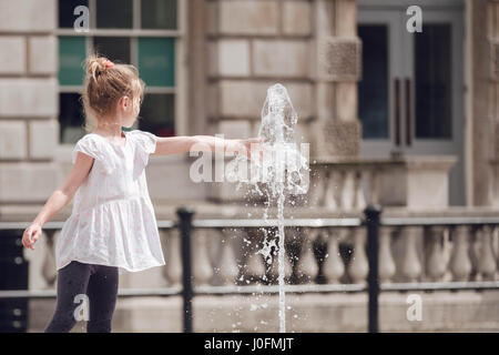 Ein junges Mädchen streckt und legt ihre Hand auf dem Wasserbrunnen am Somerset House, The Strand in London an einem heißen Sommertag im Jahr 2016. Stockfoto