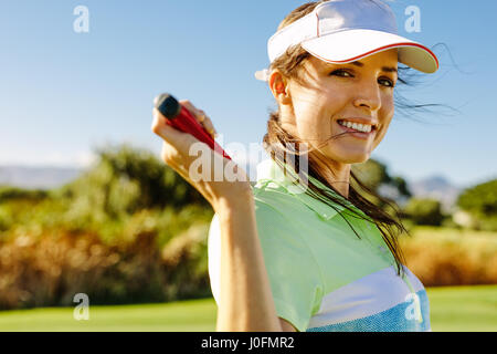 Porträt von glücklich Golfspielerin Feld Golfclub festhalten hautnah. Schöne junge Frau auf dem Golfplatz stehen und Lächeln auf den Lippen. Stockfoto