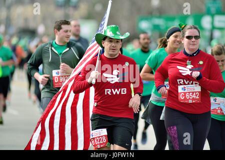 Unter einem Meer von Läufern ein Mann trägt eine amerikanische Flagge als er sich näherte, der die Ziellinie an der 2017 Shamrock Shuffle. Chicago, Illinois, USA. Stockfoto