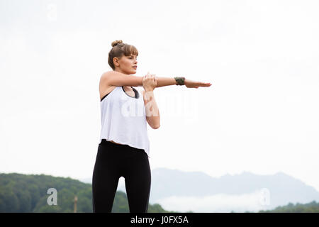 junge sportliche Frau stretching und bereitet sich irgendwo in der Natur auf den Bergen sport treiben Stockfoto
