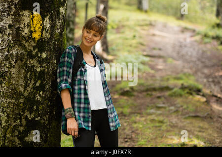 junge Frau im männlichen Karohemd, ruhen Sie sich nach einem langen Spaziergang in der Natur neben einem Baum im Wald Stockfoto