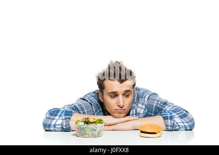 Fastfood im Vergleich zu gesunden Lebensmitteln Konzept mit jungen Mann mit vorne zwei Entscheidungen, Salat und Fast-Food, isoliert auf weiss Stockfoto