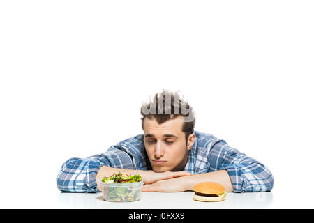 Fastfood im Vergleich zu gesunden Lebensmitteln Konzept mit jungen Mann mit vorne zwei Entscheidungen, Salat und Fast-Food, isoliert auf weiss Stockfoto