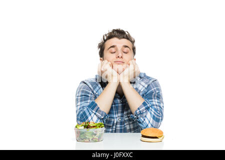 Fastfood im Vergleich zu gesunden Lebensmitteln Konzept mit jungen Mann mit vorne zwei Entscheidungen, Salat und Fast-Food, isoliert auf weiss Stockfoto