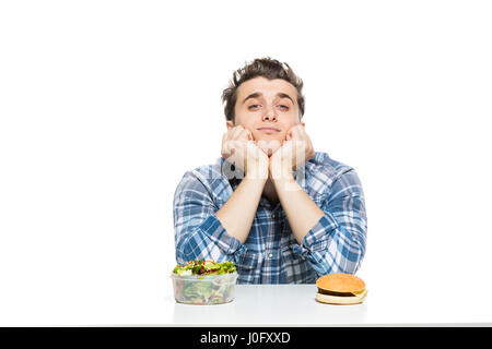 Fastfood im Vergleich zu gesunden Lebensmitteln Konzept mit jungen Mann mit vorne zwei Entscheidungen, Salat und Fast-Food, isoliert auf weiss Stockfoto