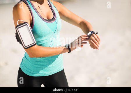 Mittelteil der Frau mit Smartwatch stehend am Strand am sonnigen Tag Stockfoto