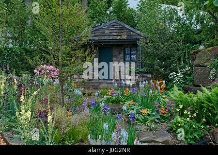 Ein Landhaus und befindet sich in einer bewaldeten Steingarten mit bunten Blumen Garten Stockfoto