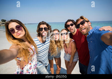 Fröhliche Freunde machen Gesicht stehen am Ufer am Strand Stockfoto