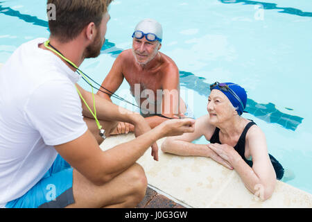 Schwimmen Sie Trainer mit Stoppuhr, älteres Paar am Pool Stockfoto