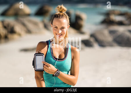 Porträt der jungen Frau berühren Smartphone auf Armbinde am Strand Stockfoto