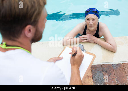 Schwimmen Sie Trainer, die Interaktion mit älteren Frau am Pool Stockfoto