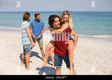 Glücklicher Mann Huckepack Freundin von Freunden am Strand Stockfoto