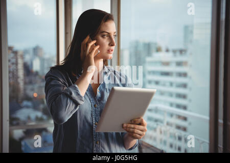 Frau am Handy mit gedrückter Tablet zu Hause Stockfoto