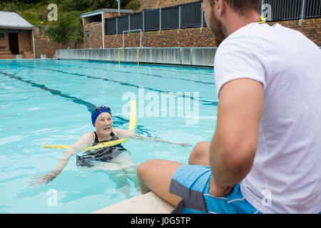 Schwimmen Sie Trainer, die Interaktion mit älteren Frau am Pool Stockfoto