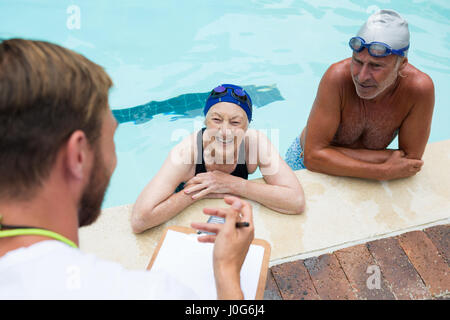 Schwimmen Sie Trainer, die Interaktion mit älteres Paar am Pool Stockfoto
