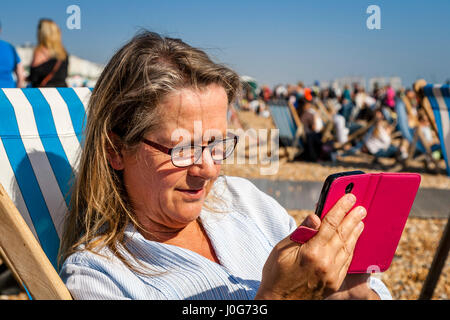 Ein applying weiblichen Blick auf ihr Smartphone, Strand von Brighton, Brighton, Sussex, UK Stockfoto