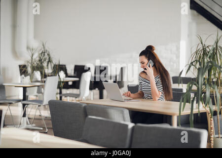 Schöne Frau an einem Tisch sitzen und am Telefon zu sprechen. Attraktive Erwachsenfrau Texteingabe auf ihrem Laptop in einem Café oder einen Arbeitsplatz. Stockfoto