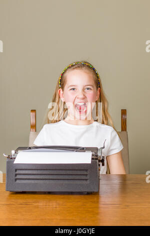 Junge blonde Mädchen wütend während der Arbeit an einer schwarzen Vintage Schreibmaschine zu Hause Stockfoto