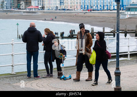 Aberystwyth Wales UK, Donnerstag, 13. April 2017 UK Wetter: Menschen zu Fuß auf der Strandpromenade promenade an einem kalten aber hellen und luftigen Tag in Aberystwyth, Wales, am Vorabend von Ostern Bank Holiday Wochenende Foto Credit: Keith Morris/Alamy Live News Stockfoto