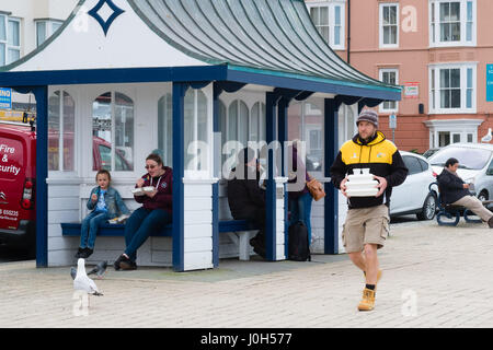 Aberystwyth Wales UK, Donnerstag, 13. April 2017 UK Wetter: Menschen essen Fisch und Chips direkt am Meer promenade an einem kalten aber hellen und luftigen Tag in Aberystwyth, Wales, am Vorabend von Ostern Bank Holiday Wochenende Foto Credit: Keith Morris/Alamy Live News Stockfoto