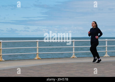 Aberystwyth Wales UK, Donnerstag, 13. April 2017 UK Wetter: eine Frau, Joggen auf der Strandpromenade an einem kalten aber hellen und luftigen Tag in Aberystwyth, Wales, am Vorabend von Ostern Bank Holiday Wochenende Foto Credit: Keith Morris/Alamy Live News Stockfoto