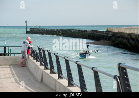 Ein Mann und eine junge zusehen, wie ein Fischerboot kehrt zum Hafen in Chichester, England. Stockfoto