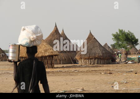 Ganyliel, Süd-Sudan. 24. März 2017. Eine Frau trägt einen Beutel mit Hilfsgütern auf dem Kopf in Ganyliel, Süd-Sudan, 24. März 2017, die Lehmhütten mit Strohdächern des Ganyliel im Hintergrund zu sehen. Foto: Jürgen Bätz/Dpa/Alamy Live News Stockfoto