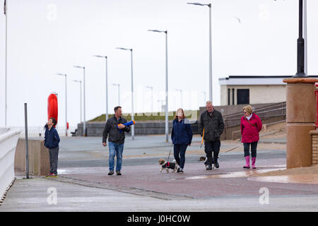 Menschen zu Fuß entlang einer nassen und windigen Promenade an der touristischen Stadt von Rhyl in Nordwales mit ihren Hunden Stockfoto