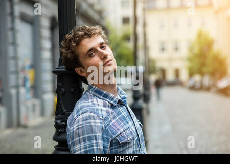 blond und lockigen Jüngling mit karierten Hemd draußen in der Nähe einen Laternenpfahl Straße Stockfoto