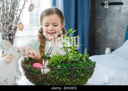 Lächelnde Mädchen Blick auf schöne blumige Ostern Komposition mit bemalten Ei Stockfoto