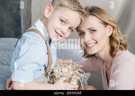 Glückliche junge Mutter und Sohn Korb mit Ostereiern lächelnd in die Kamera halten Stockfoto