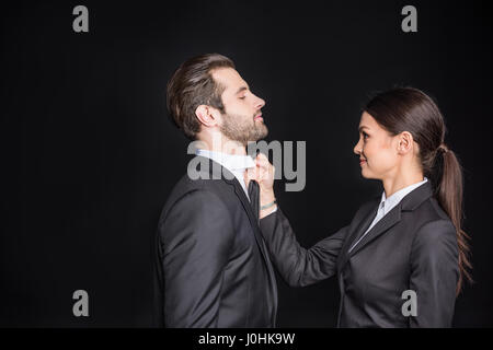 Lächelnde Geschäftsfrau Holding Geschäftsmann durch seine Krawatte auf schwarz Stockfoto