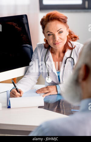 Professionelle Ärztin in Zwischenablage schreiben und mit Blick auf Patienten Stockfoto