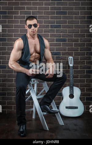 Kerl mit großen Muskeln sitzt neben der Gitarre. Stockfoto